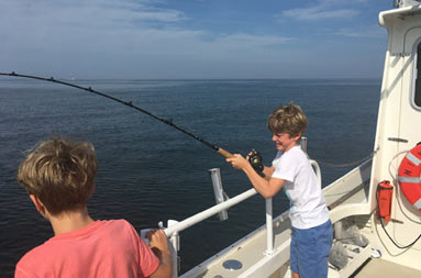 A boy holds onto his rod as he reels in a fish and another boy looks on.