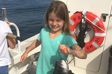 A young girl smiles and holds up the sea bass she caught.