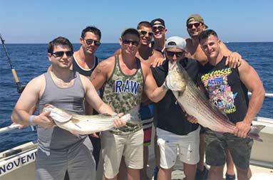 A group of 8 men pose with the striped bass they caught.