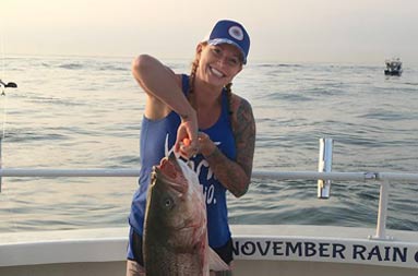 A woman wearing a blue baseball cap hat and blue tank top holds up the large fish she caught by a hook.