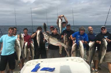 Group of 11 men each proudly hold up all the striped bass they caught.