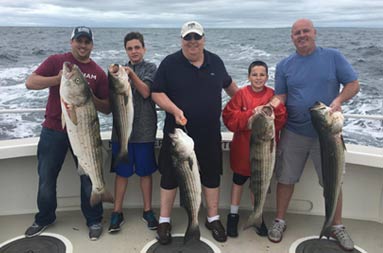 Five men and an adolescent boy smile as they each hold up the fish they caught.