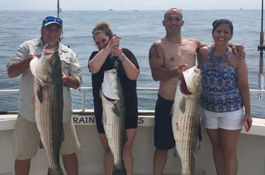 Two couples hold up the 3 striped bass they caught.