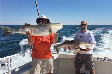 Two men smile and proudly hold up the striped bass they each caught.