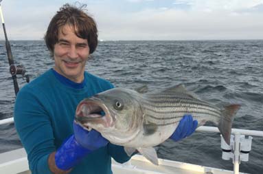 A man smiles as he holds the large bass he caught.
