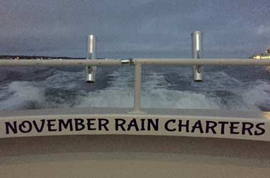 Close up of the words 'November Rain Charters' on the inside of the deck looking out at the water before dawn.