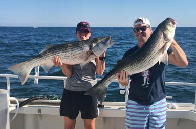 Two men each holding up the striped bass they caught.