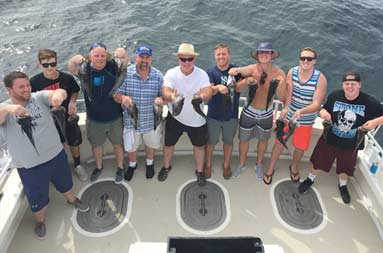 Overhead view from atop the boat looking down at the deck with 10 men looking up proudly displaying the sea bass they caught.