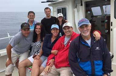 With a cloudy background, a group of 8 people sit on the boat and smile for the camera.