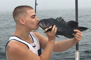 Profile view of a man holding the sea bass up to his mouth and kissing it