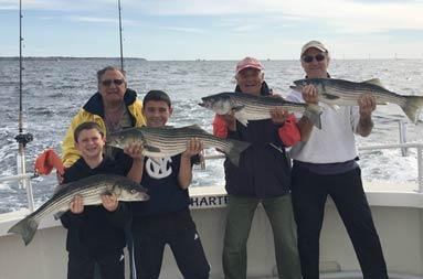 A grandfather, his two grandsons and two men smile big as they hold up 4 striped bass.