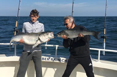A man and teenage boy each hold up a striped bass.