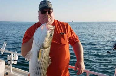 A man proudly holds up a large striped bass.