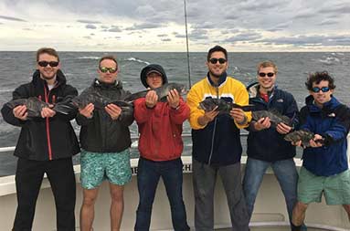 Six men standing on the boat, each holding out the sea bass they caught.