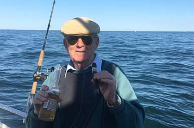With the sun casting a partial shadow on his face, a senior gentleman smiles for the camera with cigar in one hand and Corona beer in another.