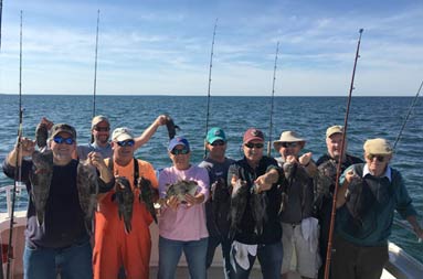 Nine men smile as they each hold up two sea bass.