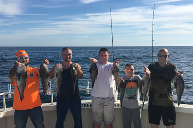 Three men, a teenage boy and younger boy each hold out the 2 sea bass they caught.