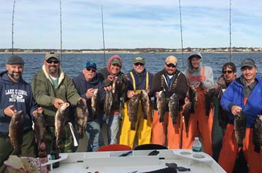 Nine men each hold up two blackfish (tautog).