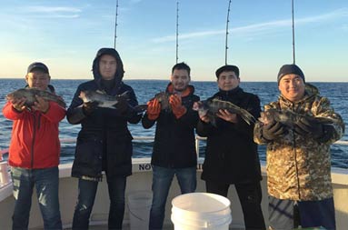 Five men smile as they each hold up one sea bass.