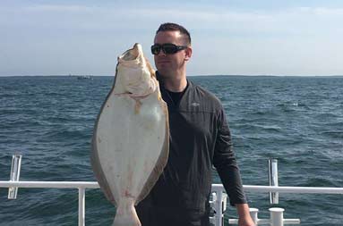 A man wearing sunglasses holds up his large fluke.