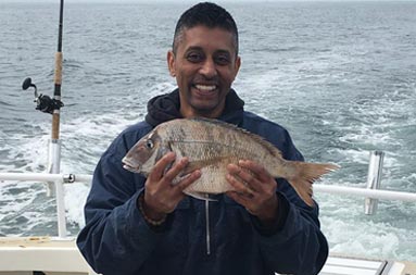 A man in a blue sweatshirt proudly holds up scup (porgy).