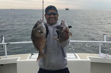 A man smiling with the water behind him as he holds up 2 porgy.