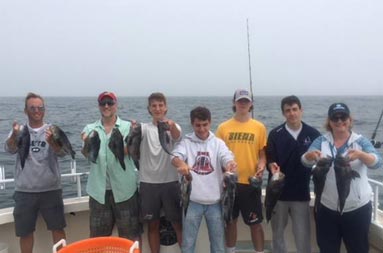 A family of 7 each hold up 2 sea bass and smile for the camera.