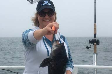 A woman smiles as she holds up a large sea bass.