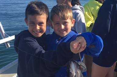 Two young boys join efforts and hold up the sea bass they caught with big smiles