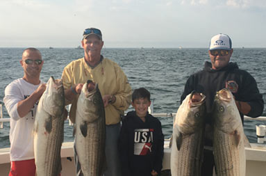Three men hold up striped bass and a young boy stands between them, all smiling.