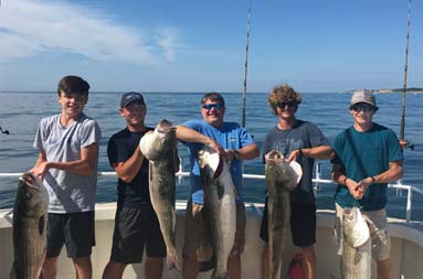 Five young-adult guys each put some extra effort into holding up their striped bass.