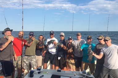 A group of 12 men smile for the cameras with some holding up sea bass.