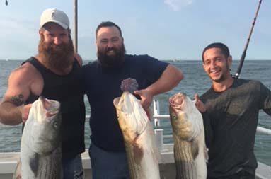 Three men smile and each hold up 3 striped bass.