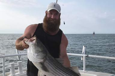 A man proudly holds up his large striped bass.