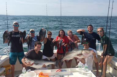 Nine men and woman proudly hold up the striped bass and sea bass they caught.