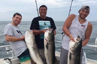 Three men smile and each hold up the striped bass they caught.