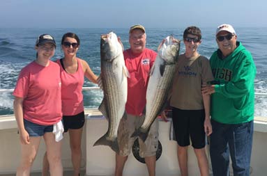 With a slightly overcast blue sky behind them, two women and three men hold up 2 striped bass.