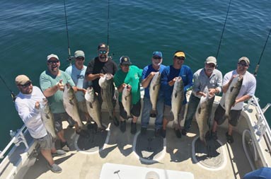 A group of men each holding up a striped bass looking up at the camera and smiling.