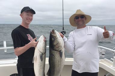 A young man and man each hold up the striped bass they caught.