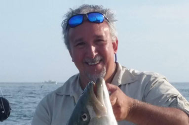 A man smiles for the camera as he holds up a large striped bass.
