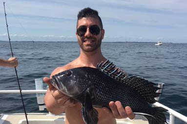 A man wearing sunglasses smiles for the camera and holds up a sea bass.