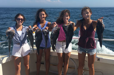Four adolescent girls smile for the camera and each hold up 2 sea bass.
