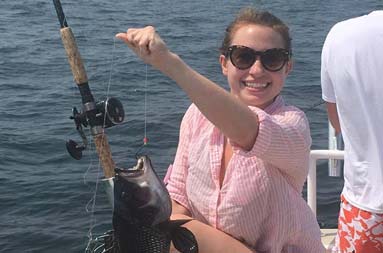 A young woman holds up her knee and smiles for the camera as she reels in a sea bass