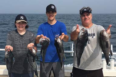 A man and two younger men each smile and hold up 2 striped bass.