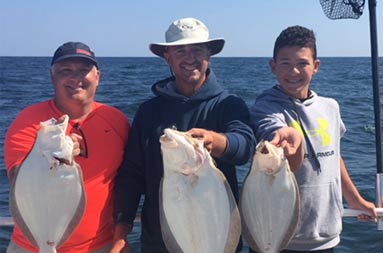 Two men and an adolescent boy each hold up fluke.