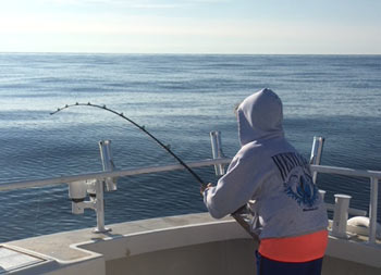 View of the back of an adolescent boy while he faces the ocean and reels in his catch.