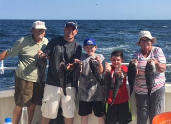 A family group consisting of grandparents, their son and his young sons smile for the camera as they each hold up sea bass.