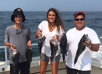 A man, young woman and young man each hold up 2 sea bass.