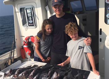 A proud father puts his hands on his son and daughter's shoulders as they look at a spread of fish they caught waiting to be filleted.