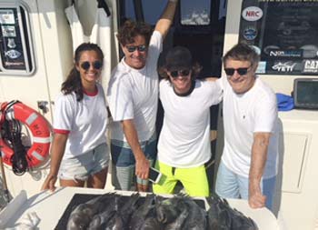 Four people stand next to the fillet board on the boat where there are sea bass laid out.